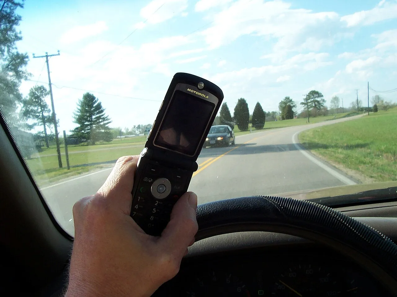 Een bestuurder die een mobiele telefoon vasthoudt tijdens het rijden.