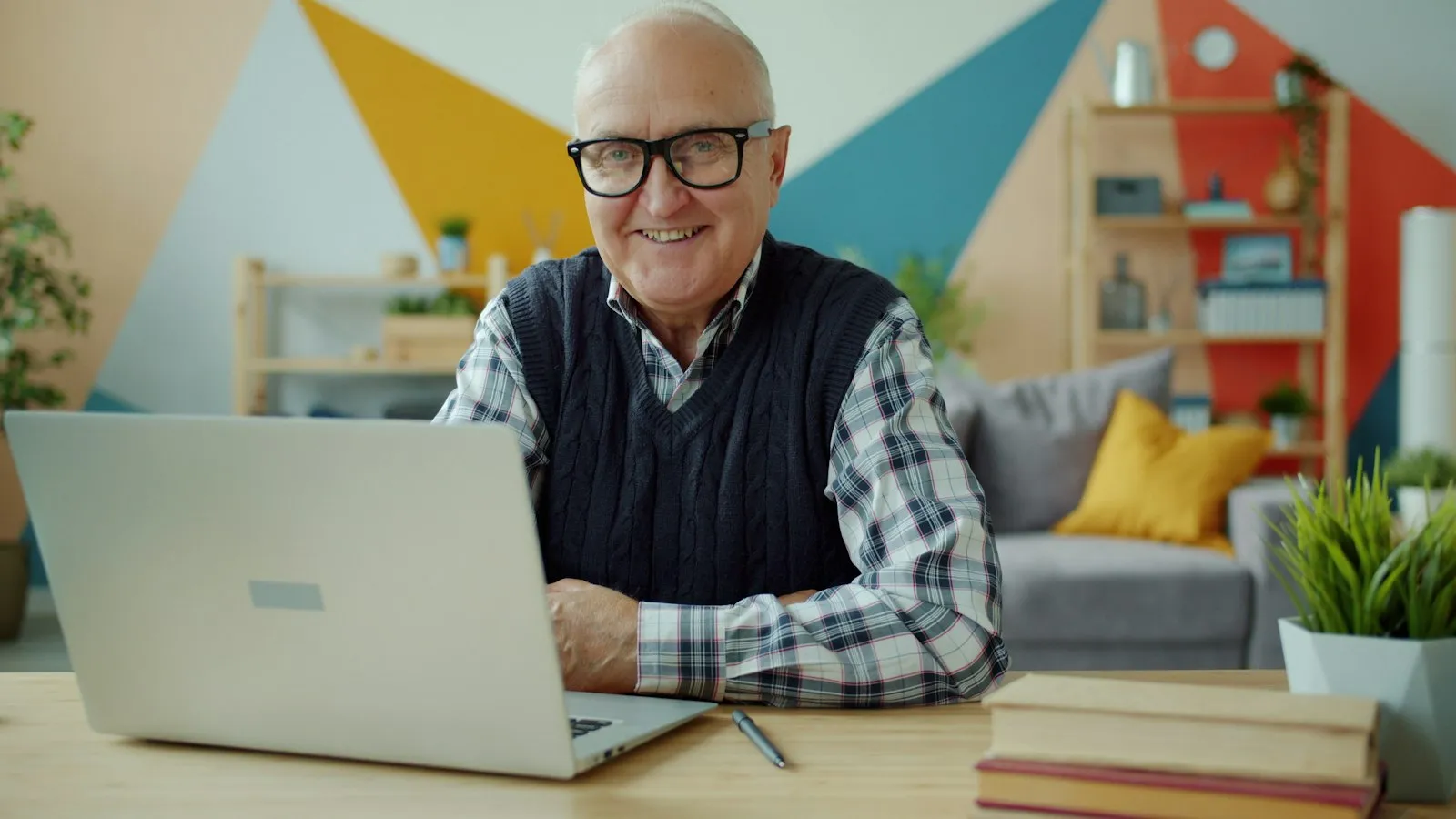 Lachende oudere man met bril die achter een laptop werkt